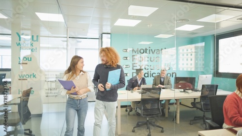 Colleagues with folders chatting in a bright office environment.