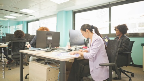 Focused employees working at desks in a bright office with glass walls.