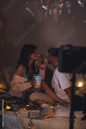 Romantic surprise for girlfriend or boyfriend. Bedroom prepared for watching old movies with popcorn, decorated with lights and candles. Cozy home Christmas atmosphere, hot chocolate with marshmallow