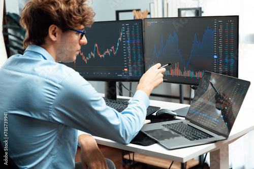 Young investor in stock trader pointing on dynamic exchange rate on laptop and pc screen in dynamic market graph online in real time at modern home office, analyzing financial technology data. Gusher.