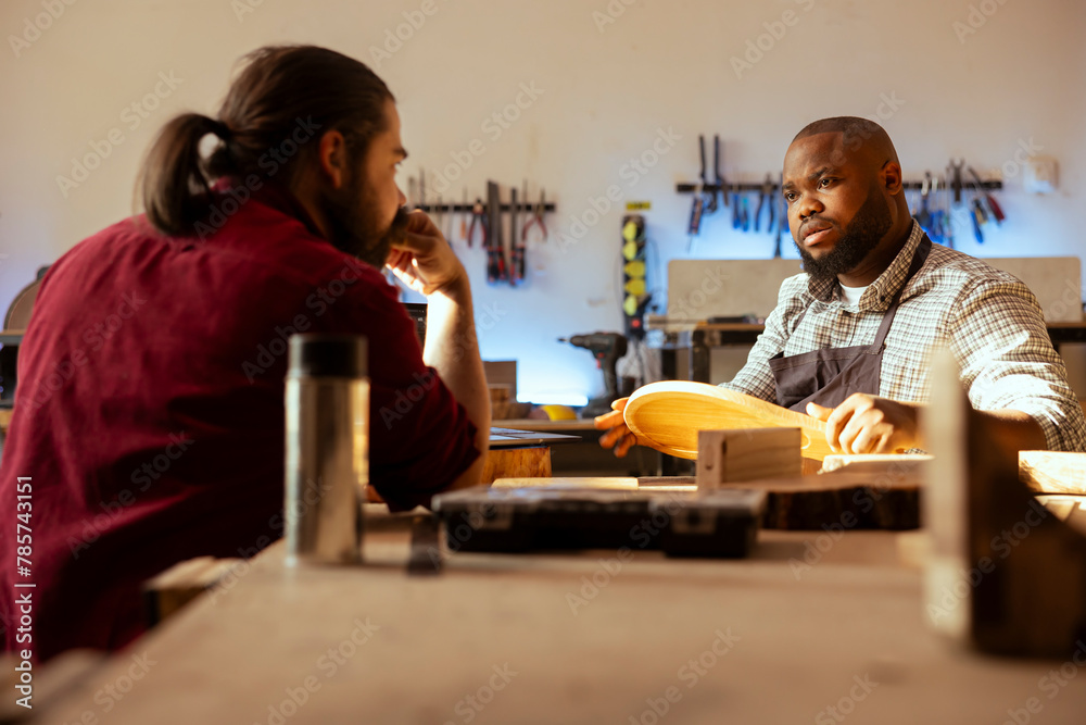 Manufacturer and apprentice discussing in studio to select best wood materials for project. Cabinetmaker and colleague talking in joinery, doing quality assurance on lumber piece Manufacturer and apprentice discussing in studio to select best wood materials for project. Cabinetmaker and colleague talking in joinery, doing quality assurance on lumber piece
