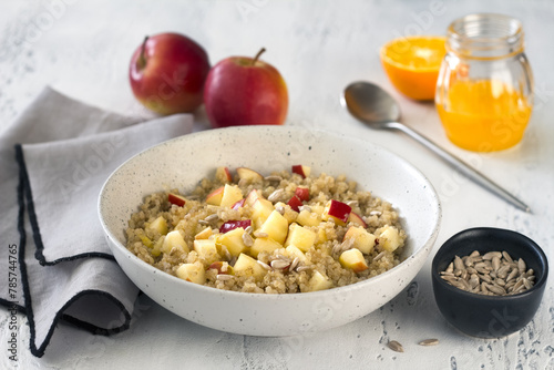Quinoa with apples, sunflower seeds, honey and orange juice on a light blue table. Vegan healthy dish