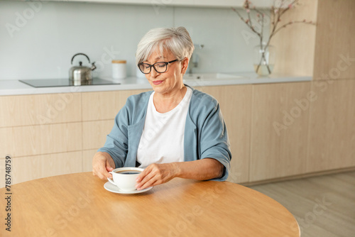 Good morning. Comfort relaxed senior old elderly woman grandmother drinking hot beverage tea coffee in kitchen at home. Mature woman resting enjoy calm morning at modern home alone. Pension concept