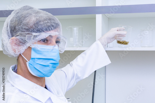 Cientista usando equipamento de proteção em laboratório segura béquer com cápsulas para analize. photo