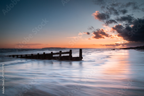 Long exposure landscape photograph at Camber sands beach on a warm evening, Image shows the beautiful sunset and glowing sky with a damaged wooden groyne subject and a receding tide photo