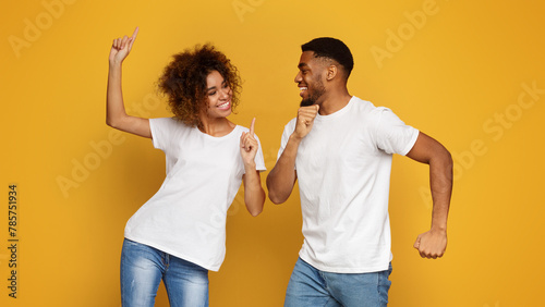 Positive black guy and girl dancing on orange background