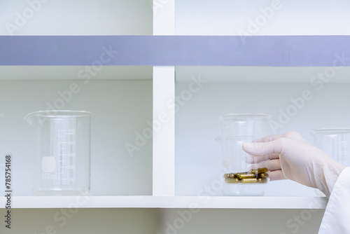 Mão de cientista segura béquer com cápsulas em laboratório de pesquisa.