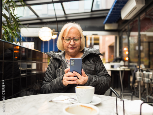 pov senior woman looking at cell phone with coffees already finished