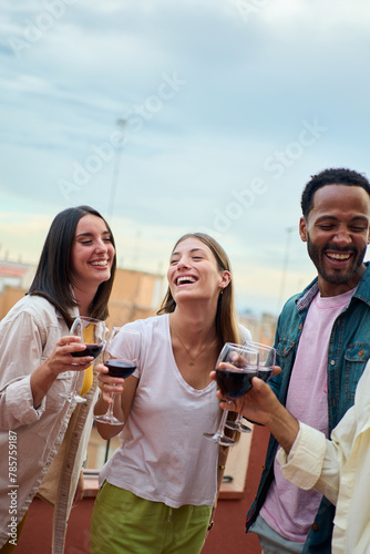 Vertical. Cheerful group multiracial young friends laughing holding wine glass at summer rooftop party. Gathering joyful millennial people enjoying together smiling having fun on vacation outdoors