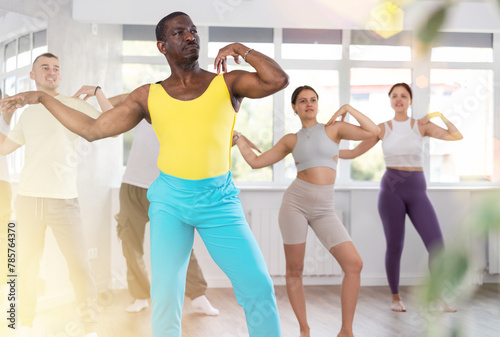 African man conducts lesson for multinational people company, teaches men and woman to move aesthetically to beat of music, control their bodies and perform modern energy contemporary dance