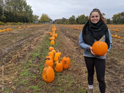 A young woman holds a pumpkin at a pumpkin patch in the fall