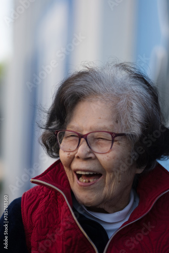 An elderly grandmother lets out a big laugh while dining outdoors. She is over ninety years old, of Okinawan (Ryukyuan) descent, and living with dementia.