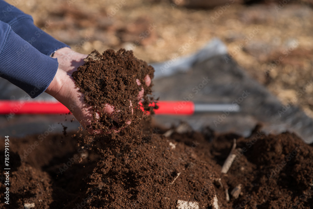 Hands in rich soil compost above tarp outdoors. Right hand in focus, closer to camera. Hands in rich soil compost above tarp outdoors. Right hand in focus, closer to camera.