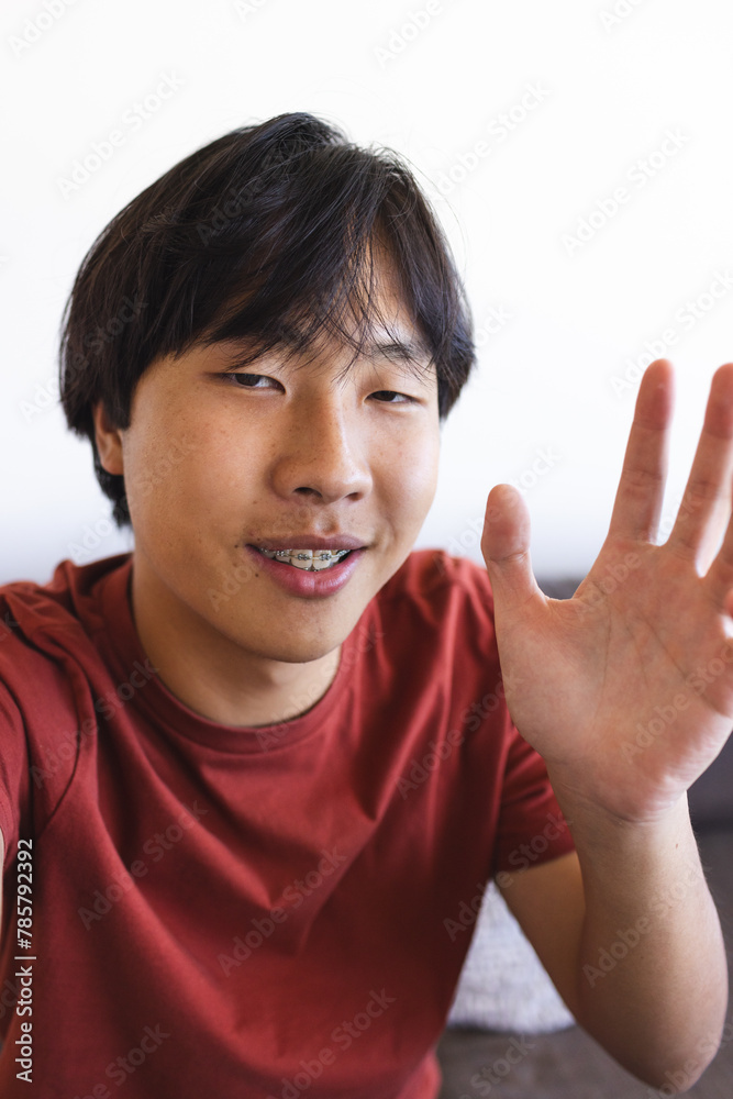 Asian teenage boy waving during a video call at home, sitting indoors Asian teenage boy waving during a video call at home, sitting indoors