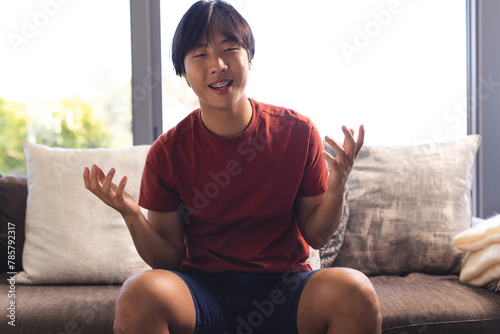 Asian teenage boy sitting on a couch at home, having a video call, talking and gesturing
