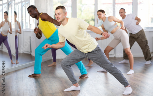Positive guy engaged in hip-hop dance together with other attendees of dancing courses