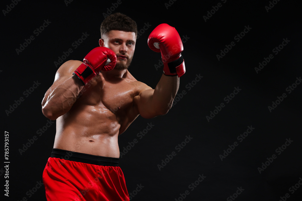 Man in boxing gloves fighting on black background. Space for text