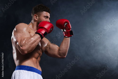 Man wearing boxing gloves fighting in smoke on black background, low angle view. Space for text