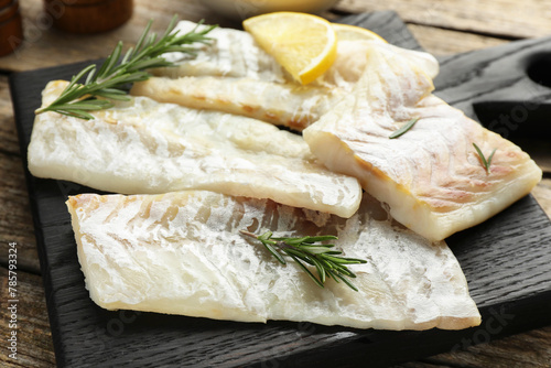 Fresh raw cod fillets with rosemary and lemon on wooden table, closeup