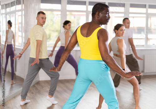 Dynamic middle-aged guy training aerobic dance poses in dancehall during workout session