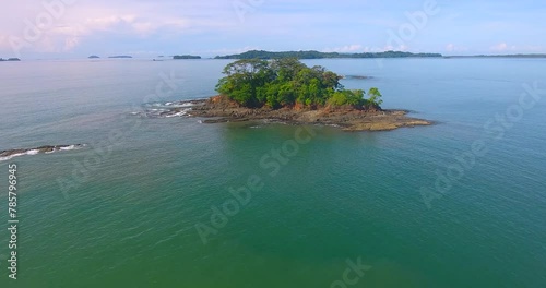 Slowly approaching a little barron island covered in rough rocky terrain and a small forest of trees near Boca Chica, Panama photo