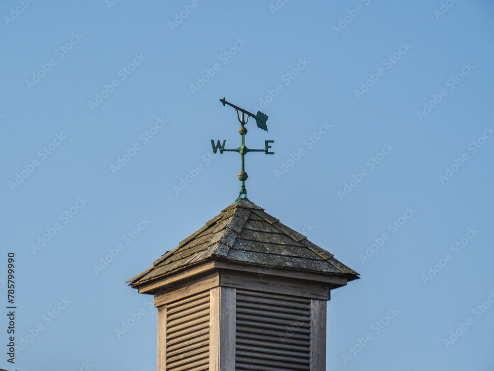 a simple arrow weather vane pointing West on a shingled roof copula on a country building