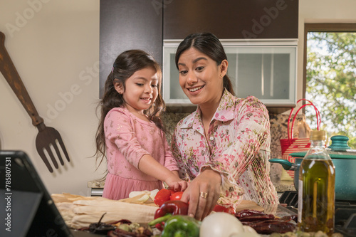 Mother takes some vegetables to process while teaching her daughter how to prepare food in the kitchen.