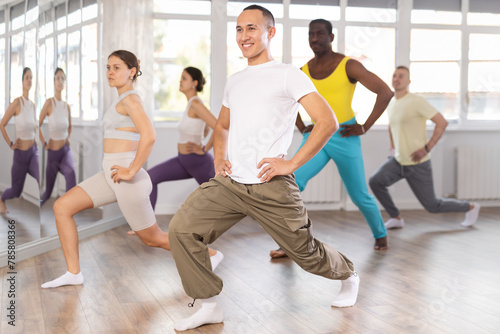 Dynamic Asian guy stretching legs in training room during workout session