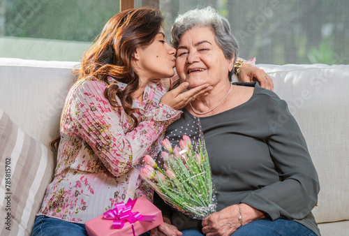 Daughter kisses her mother on the cheek and gives her a beautiful bouquet of flowers