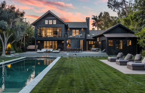 A stunning black modern farmhouse with an elegant pool and lush green backyard, with perfectly manicured grass and stylish outdoor furniture.