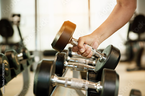 Close up hand holding dumbbell on floor in gym with woman background. Object goal weightlifting bodybuilding.