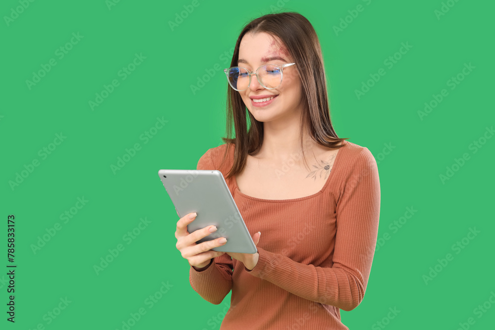 Young woman in eyeglasses using tablet computer on green background