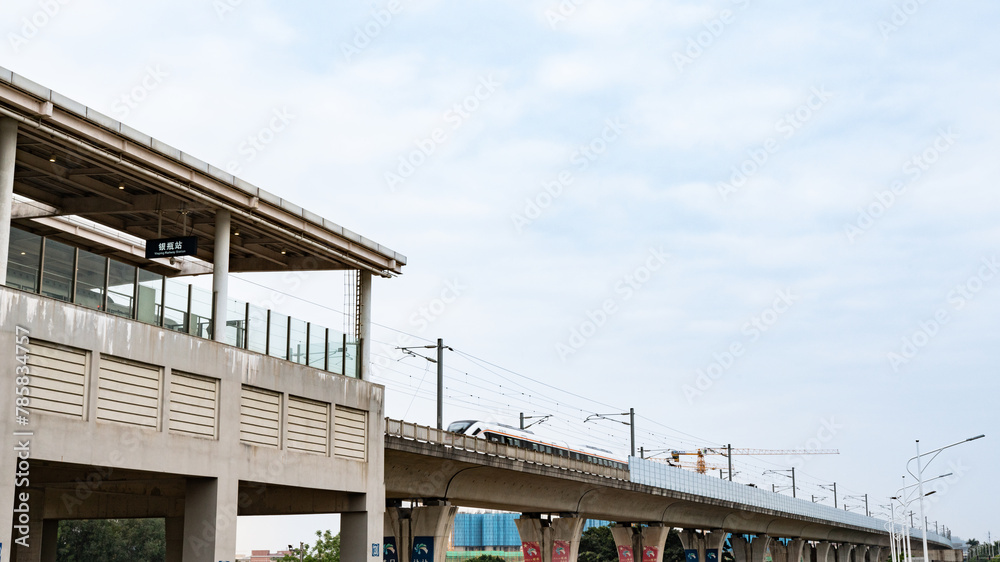 Xiegang Town, Dongguan City, Guangdong Province, China, Yinpian Station, a light rail and urban rail station, under the blue sky and white clouds, with high-speed trains running on the tracks.