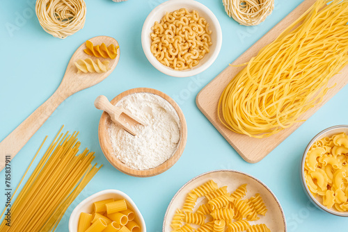 Bowls with different uncooked pasta on blue background