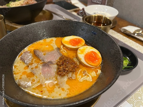 A bowl of Japanese Tonkotsu Ramen with egg, smoked beef and spicy creamy broth. Served with green tea and some garnish