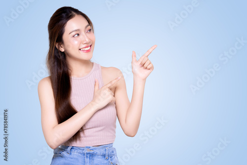 Asian Smiling woman pointing finger to the side isolated on blue background with copy space.