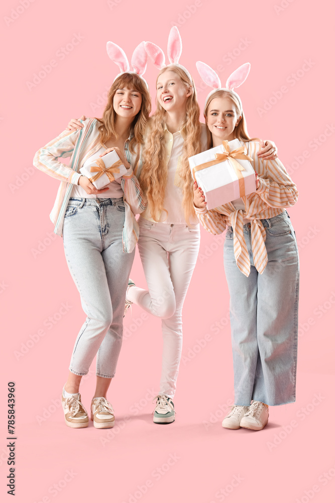 Young girls with bunny ears celebrating Easter on pink background