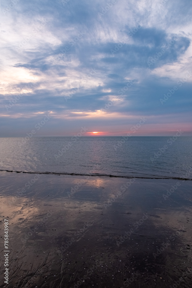 This photograph captures the tranquil beauty of early morning with the sunrise gently gracing the ocean's horizon. The quiet play of light and shadow across the clouds and the soft reflection on the