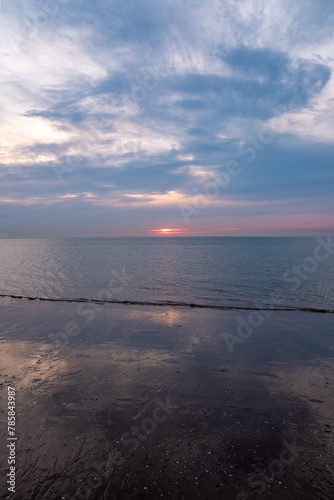 This photograph captures the tranquil beauty of early morning with the sunrise gently gracing the ocean s horizon. The quiet play of light and shadow across the clouds and the soft reflection on the