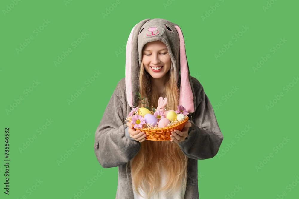 Beautiful young happy woman in bunny costume with basket full of eggs and flowers on green background. Easter celebration Beautiful young happy woman in bunny costume with basket full of eggs and flowers on green background. Easter celebration