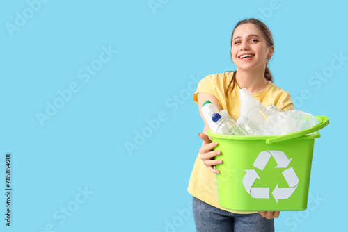 Young woman holding recycle bin with plastic garbage on blue background. Waste sorting concept
