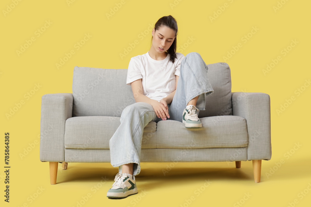 Tired young woman sitting on sofa against yellow background Tired young woman sitting on sofa against yellow background