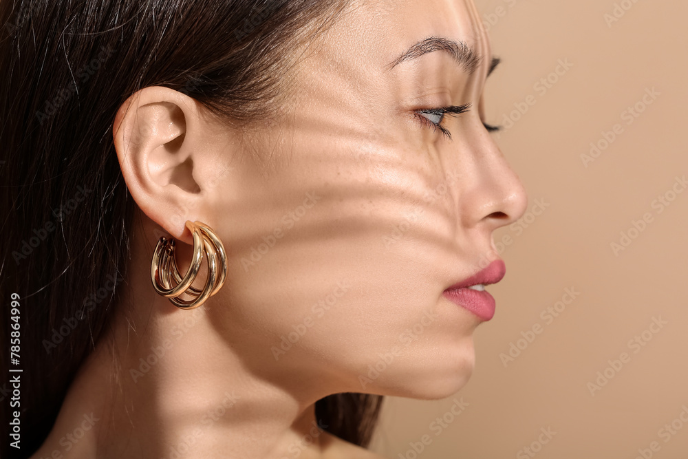 Young woman with beautiful earrings on beige background, closeup