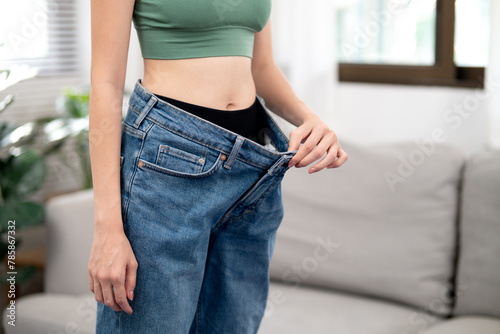 young woman pulling her pants waist with her hand showing that she is thinner