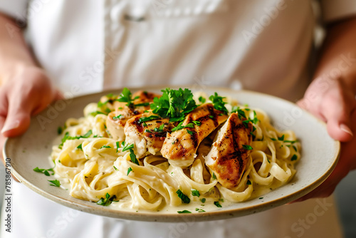 A person is holding a plate of chicken and pasta