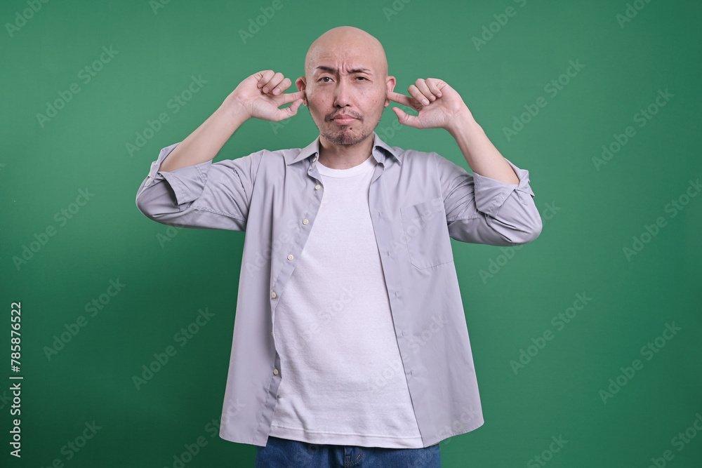 Bald man covering ears with fingers isolated on green background. Bald man covering ears with fingers isolated on green background.