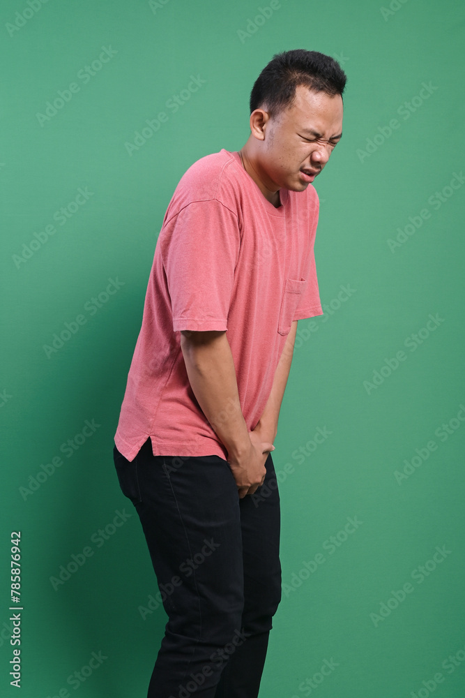 Young man with hands holding his crotch isolated on green background. Sick man prostate cancer concept.