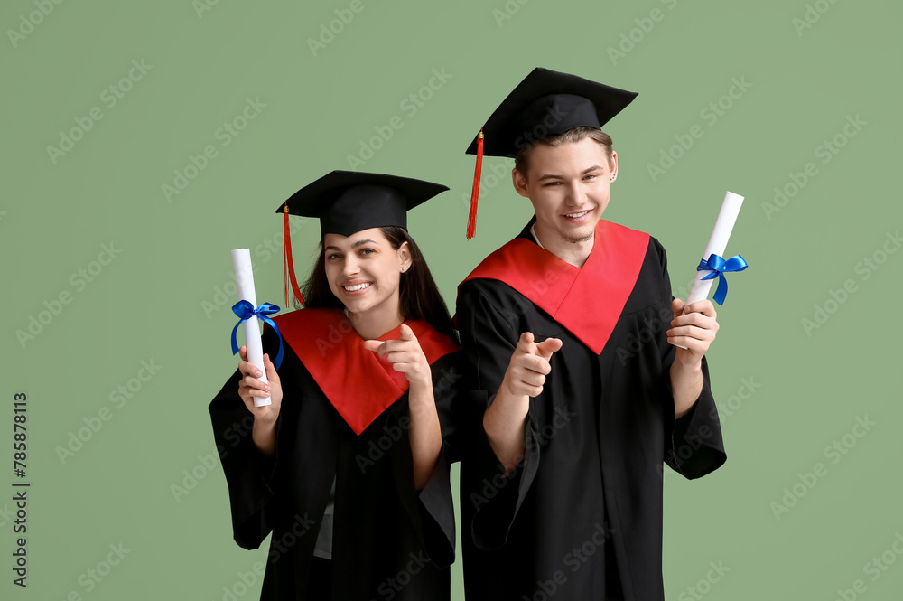 Happy graduate couple with diplomas pointing at viewer on green background Happy graduate couple with diplomas pointing at viewer on green background