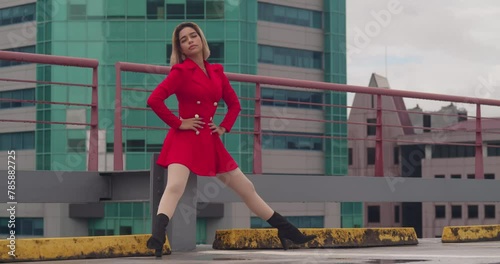 In Port of Spain, Trinidad, a young Hispanic girl sits on a rooftop in a red dress, with tall buildings in the distance. photo