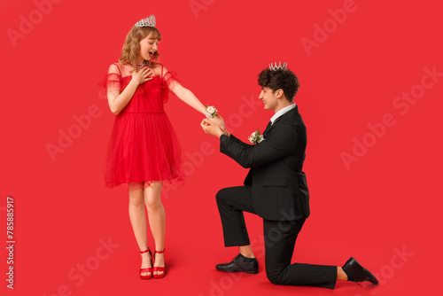 Young boy tying corsage around his prom date's wrist on red background